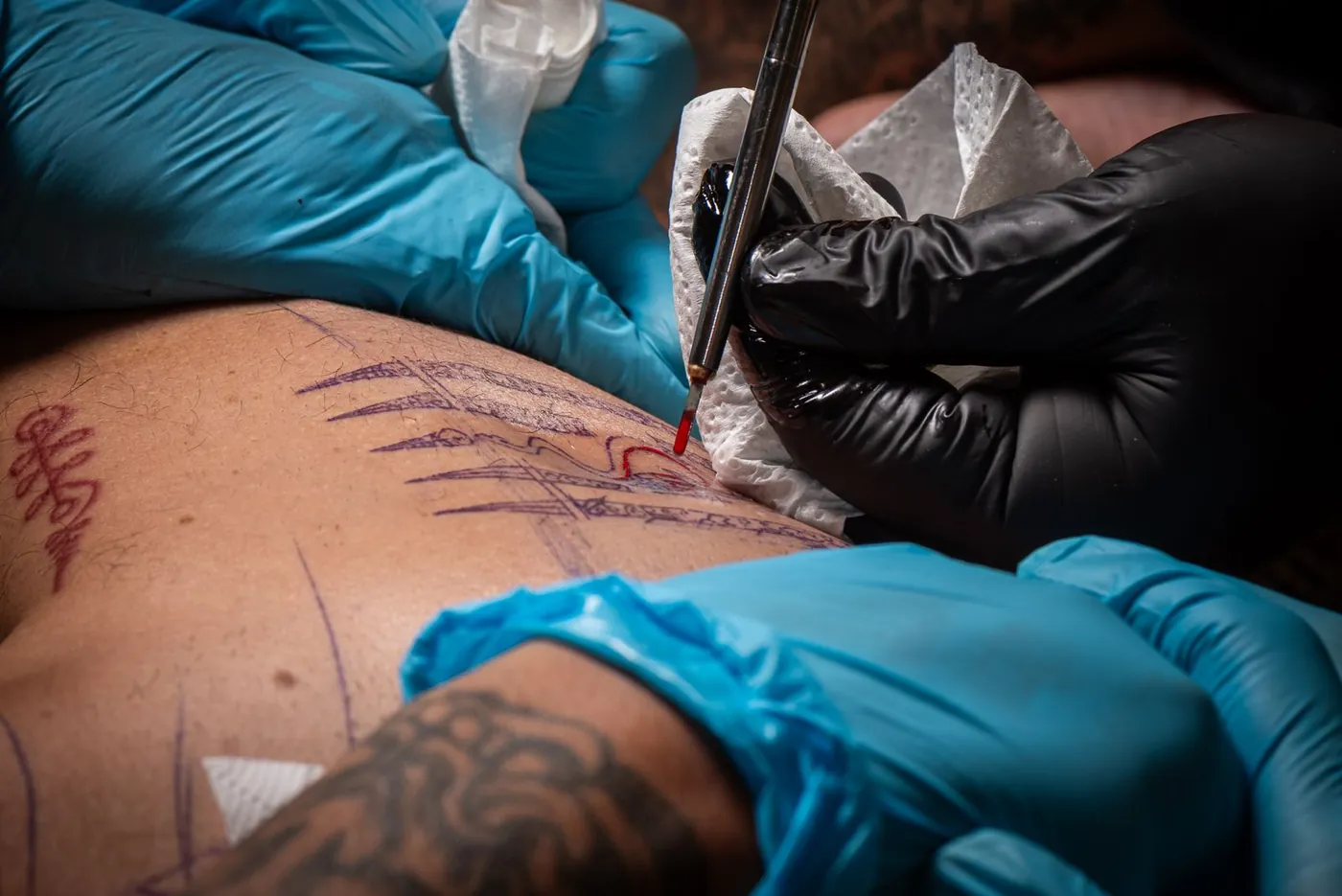 Gloved hands hand-poking a Sak Yant