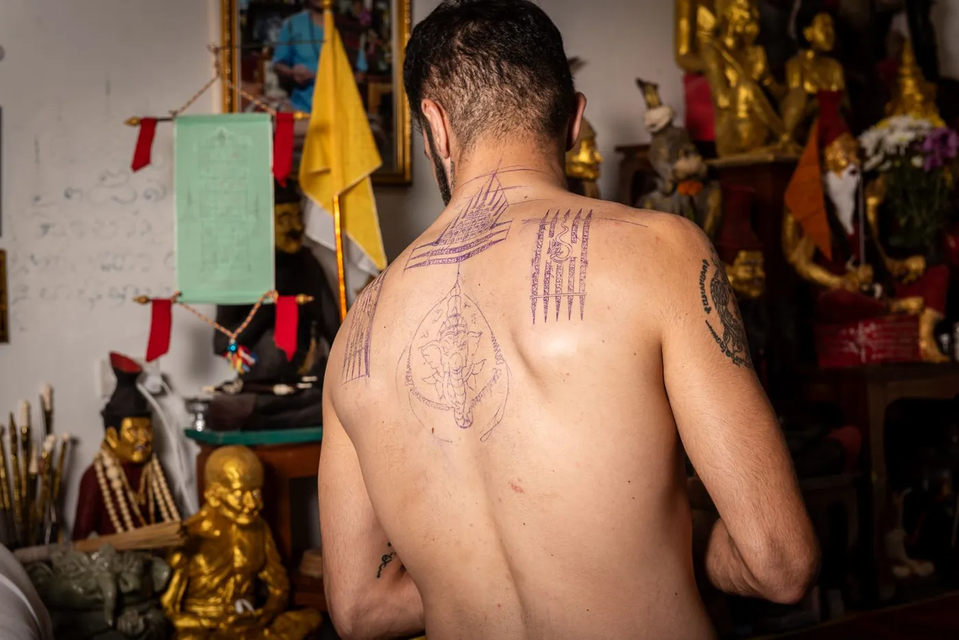 A client before the shrine with his Sak Yant design drawn on his back